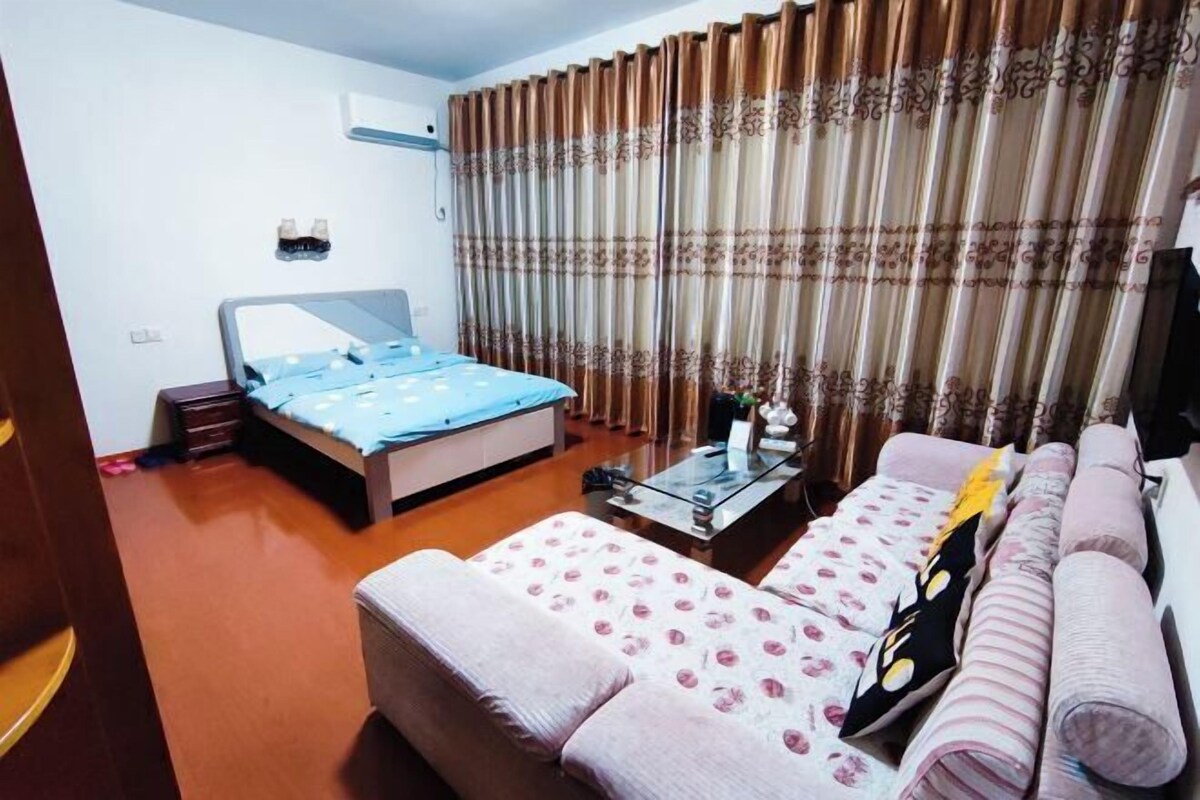 A bedroom with a bed, a sofa, a coffee table, and curtains.