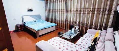 A bedroom with a bed, a sofa, a coffee table, and curtains.