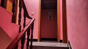Una escalera con barandilla de madera que conduce a una habitación con paredes rosas y un cuadro en la pared.