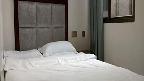 A neatly made bed with white linens in a room with a padded headboard and a window with curtains. - Yijia Inn (Chongqing)