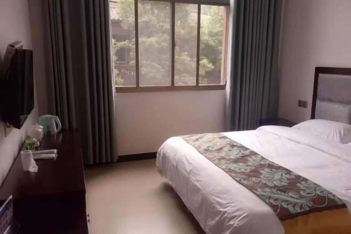 A hotel room with a bed, a desk with a kettle, and a window with curtains.