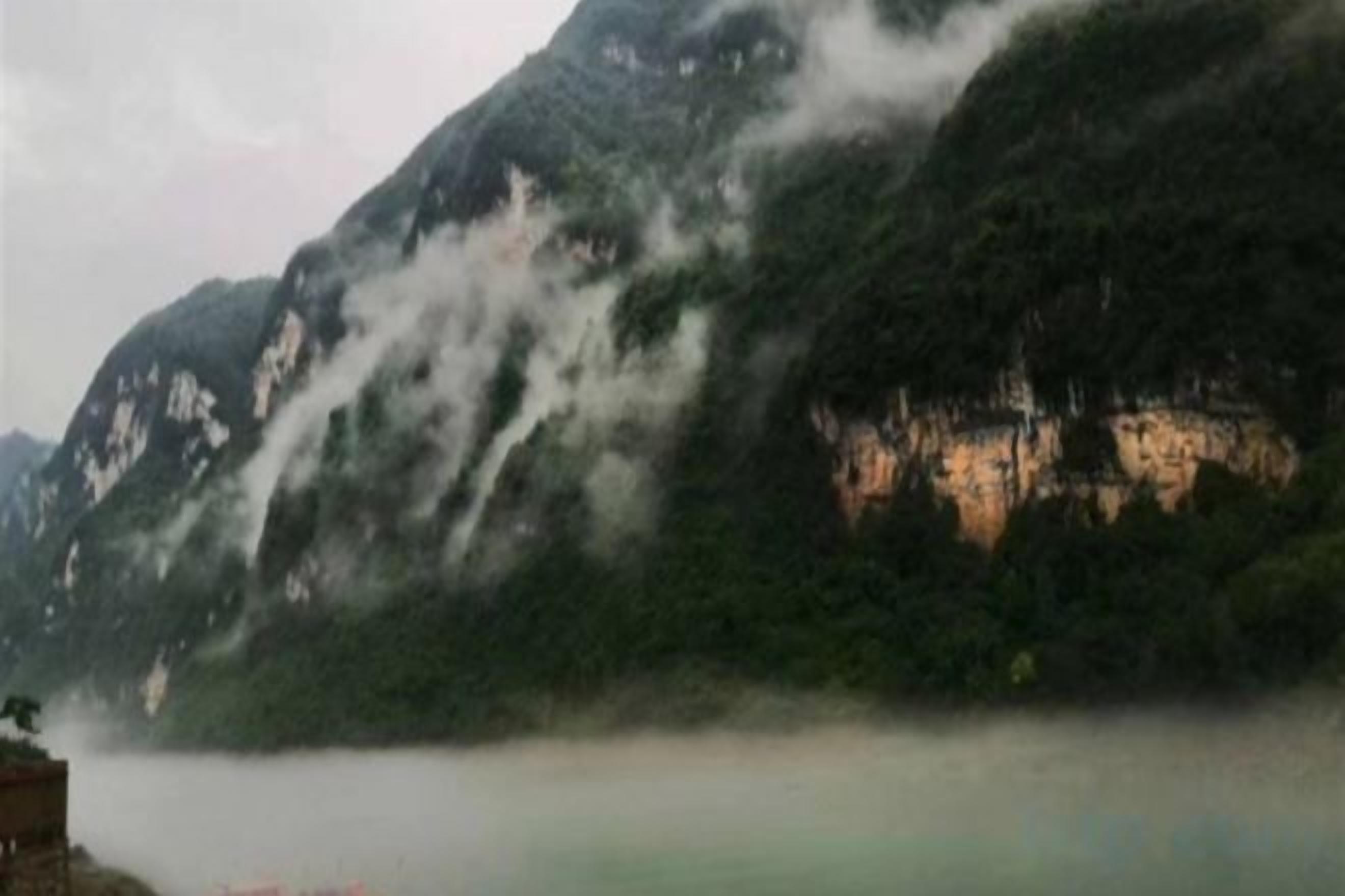 Un paisaje montañoso con un cuerpo de agua al frente y un edificio a la izquierda.