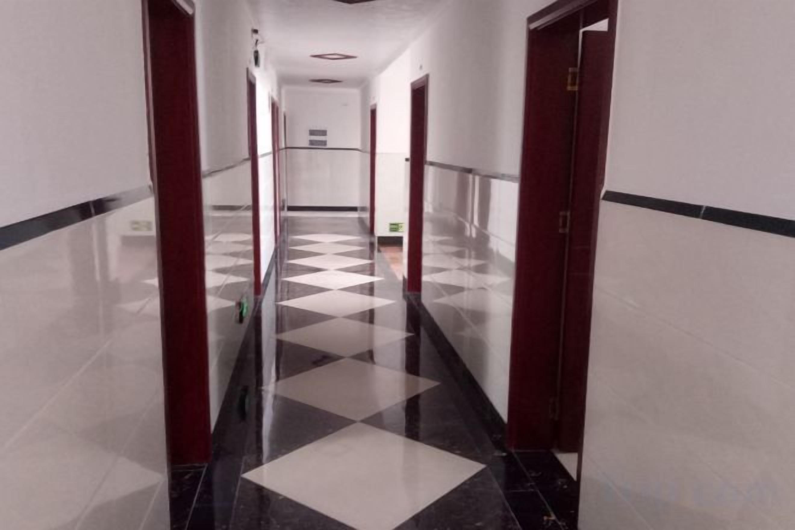 A corridor with a checkered floor pattern, doors on both sides, and a ceiling with recessed lighting.