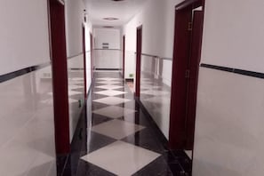 Un couloir dont le sol est recouvert d’un motif à carreaux, avec des portes de part et d’autre, et un plafond doté d’un éclairage encastré.