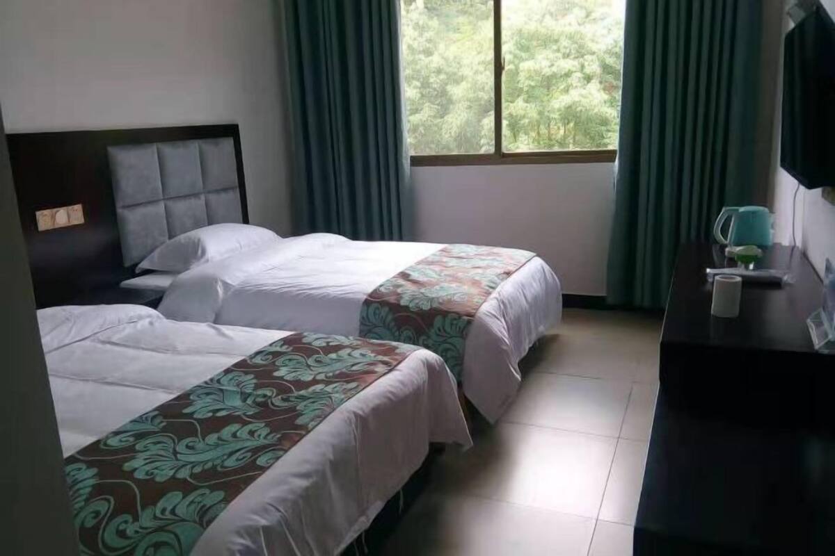 A hotel room with two beds, a desk, a TV, and a window with curtains.