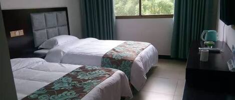 A hotel room with two beds, a desk, a TV, and a window with curtains.