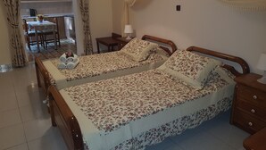 Une chambre avec deux lits, une tête de lit en bois, une table de chevet, une lampe et une vue sur un coin repas avec une table et des chaises.