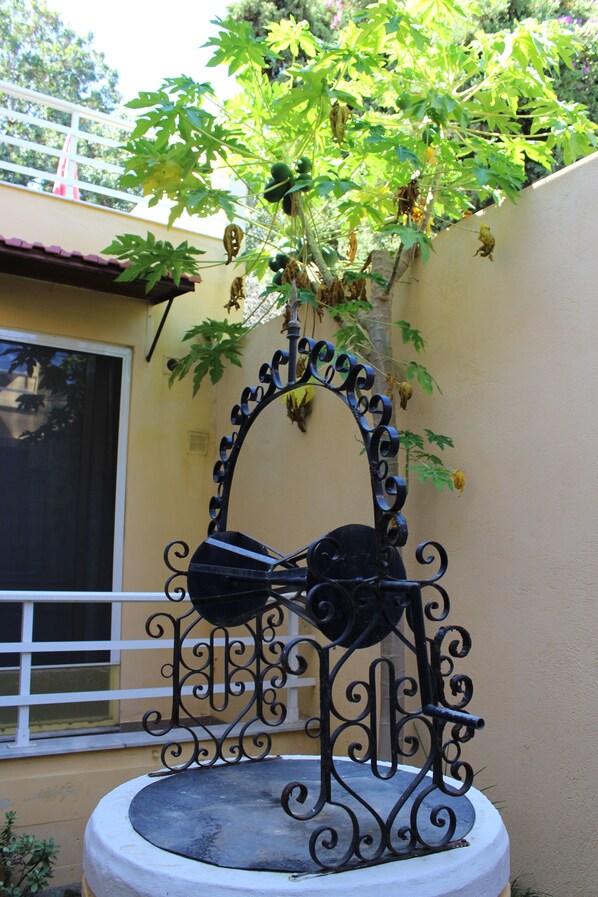 A decorative metal fountain with a plant growing over it, set against a building wall.