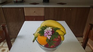 Un comptoir de cuisine sur lequel se trouve un panier de fruits contenant des bananes, une pomme, une orange et des fleurs.