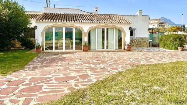 Um edifício com telhado de telhas, grandes portas de vidro e entrada pavimentada em pedra.