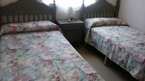 Quarto com duas camas de solteiro, mesa de cabeceira com abajur e janela que proporciona luz natural.