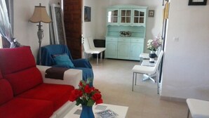 Uma sala de estar com um sofá vermelho, um vaso azul com flores e um armário azul-claro ao fundo.