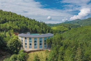 Un hôtel circulaire à plusieurs étages, entouré d’une forêt dense et de collines.