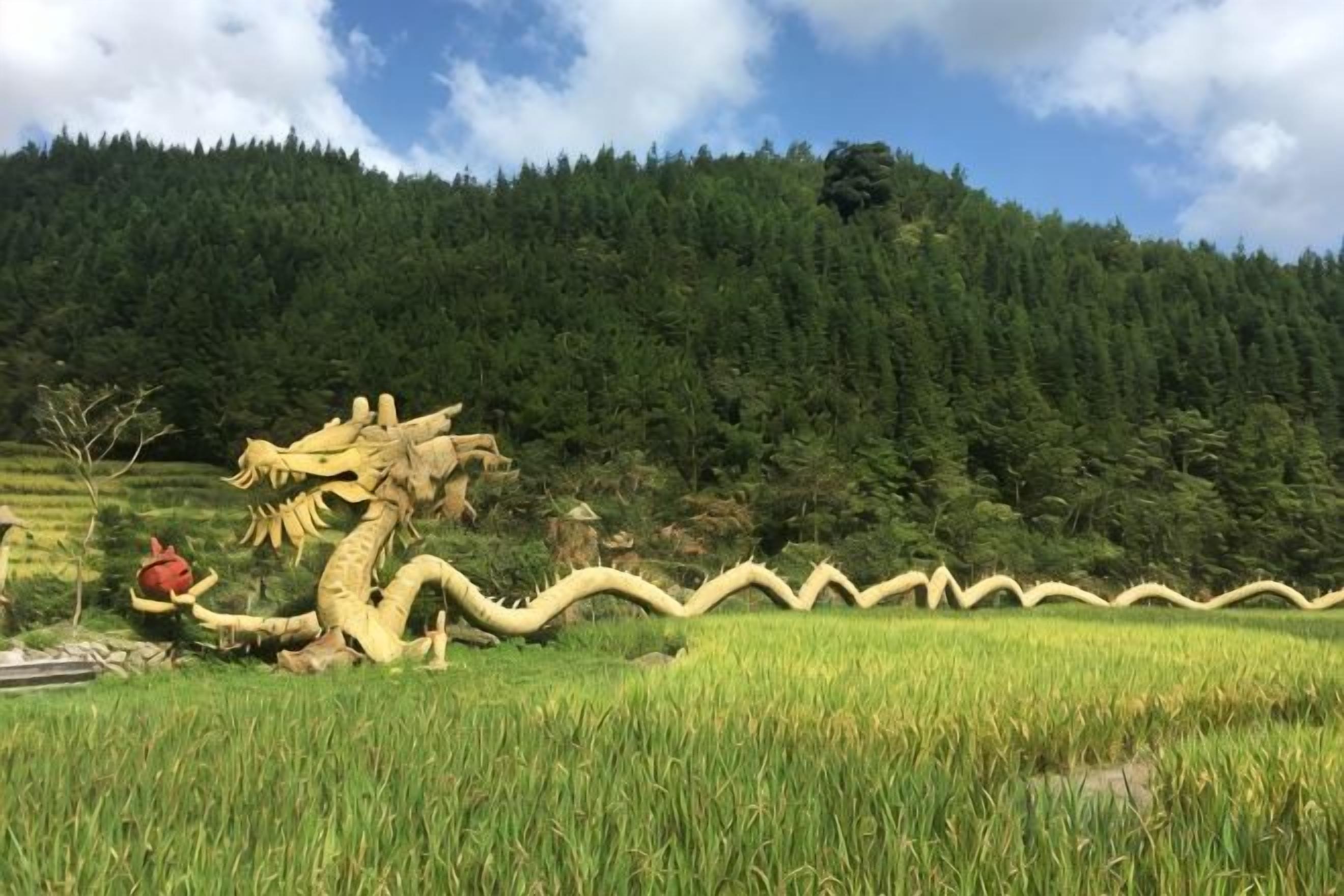 A dragon sculpture in a field with a forested hill in the background.