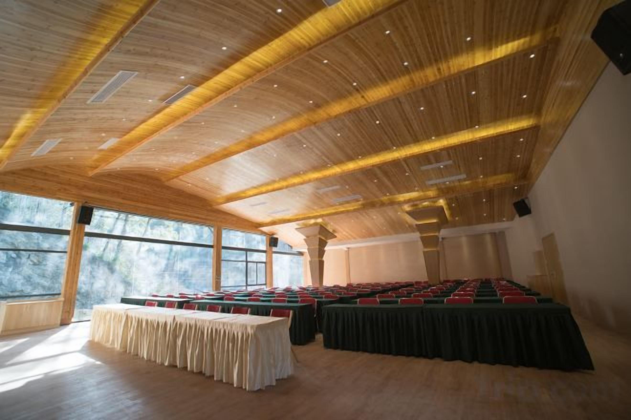 A conference room with a high ceiling, large windows, and a long table set for meetings.