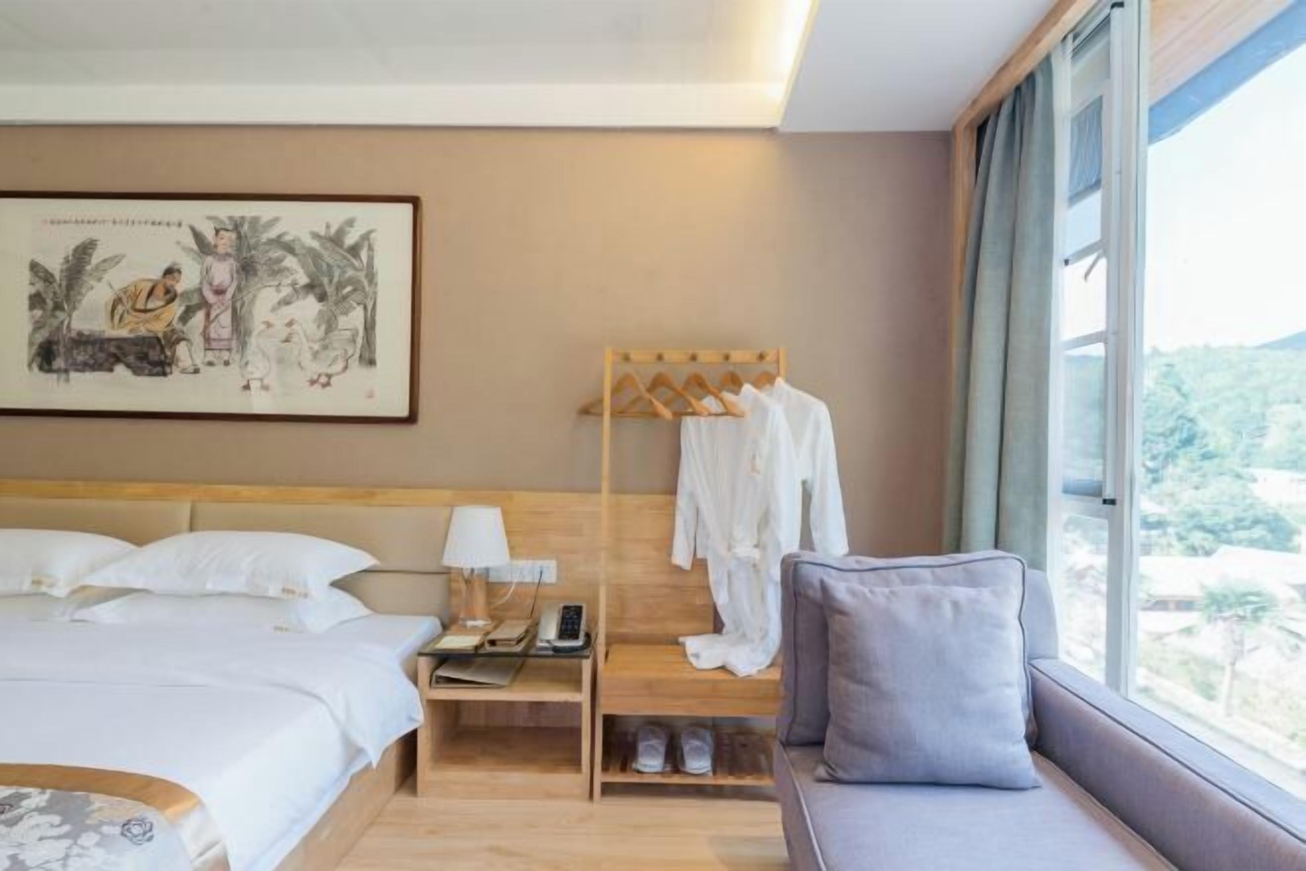 Habitación de hotel con cama, mesita de noche, lámpara, perchero para bata y vistas al exterior.