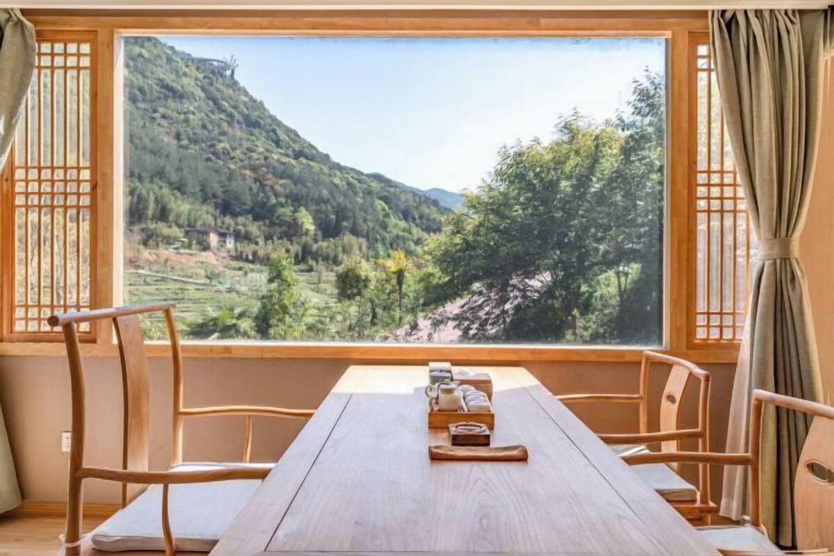 Ein Zimmer mit einem Holztisch, zwei Stühlen und einem großen Fenster mit Blick auf eine Berglandschaft.
