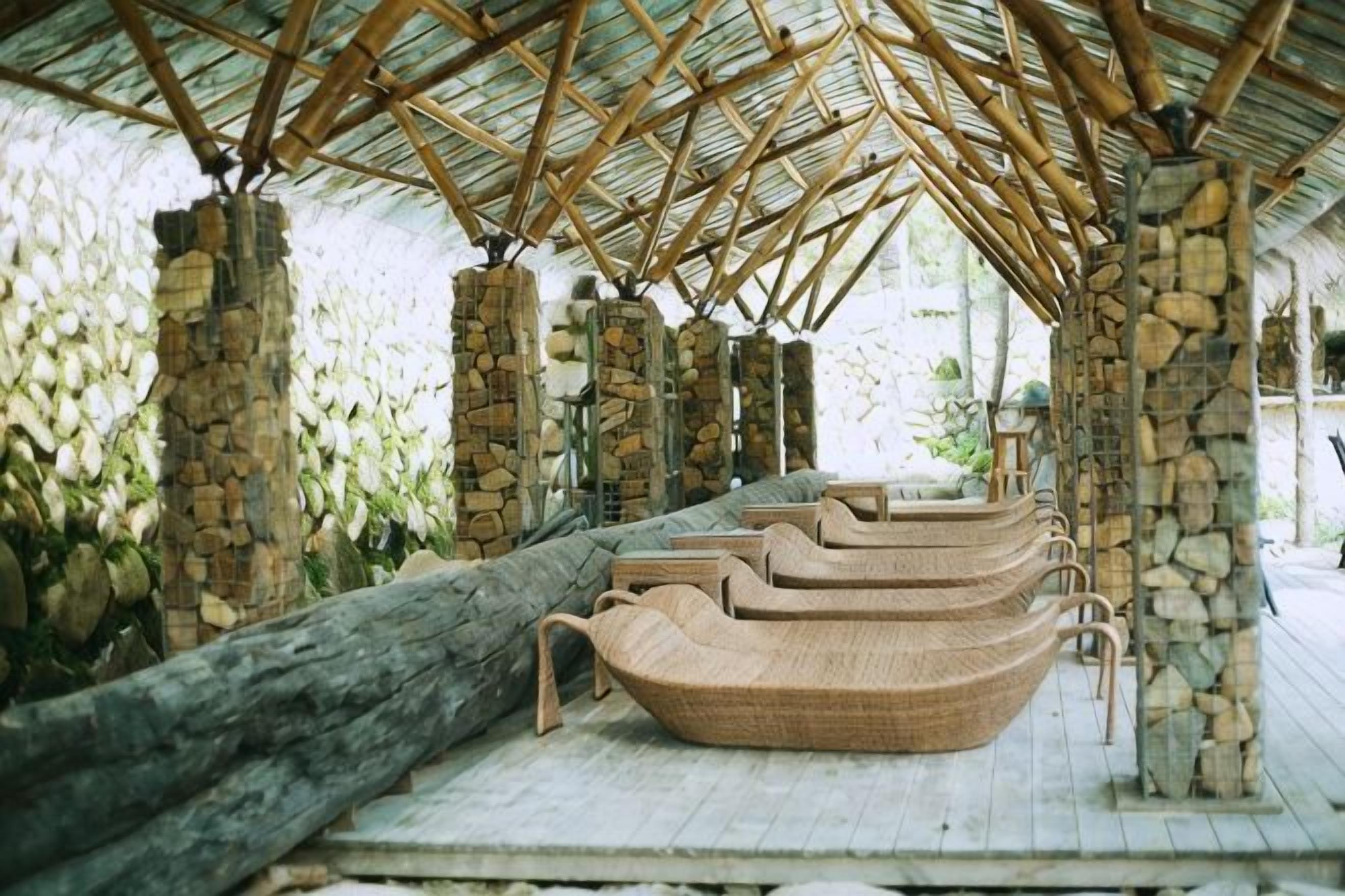 A covered outdoor seating area with stone pillars and woven chairs.