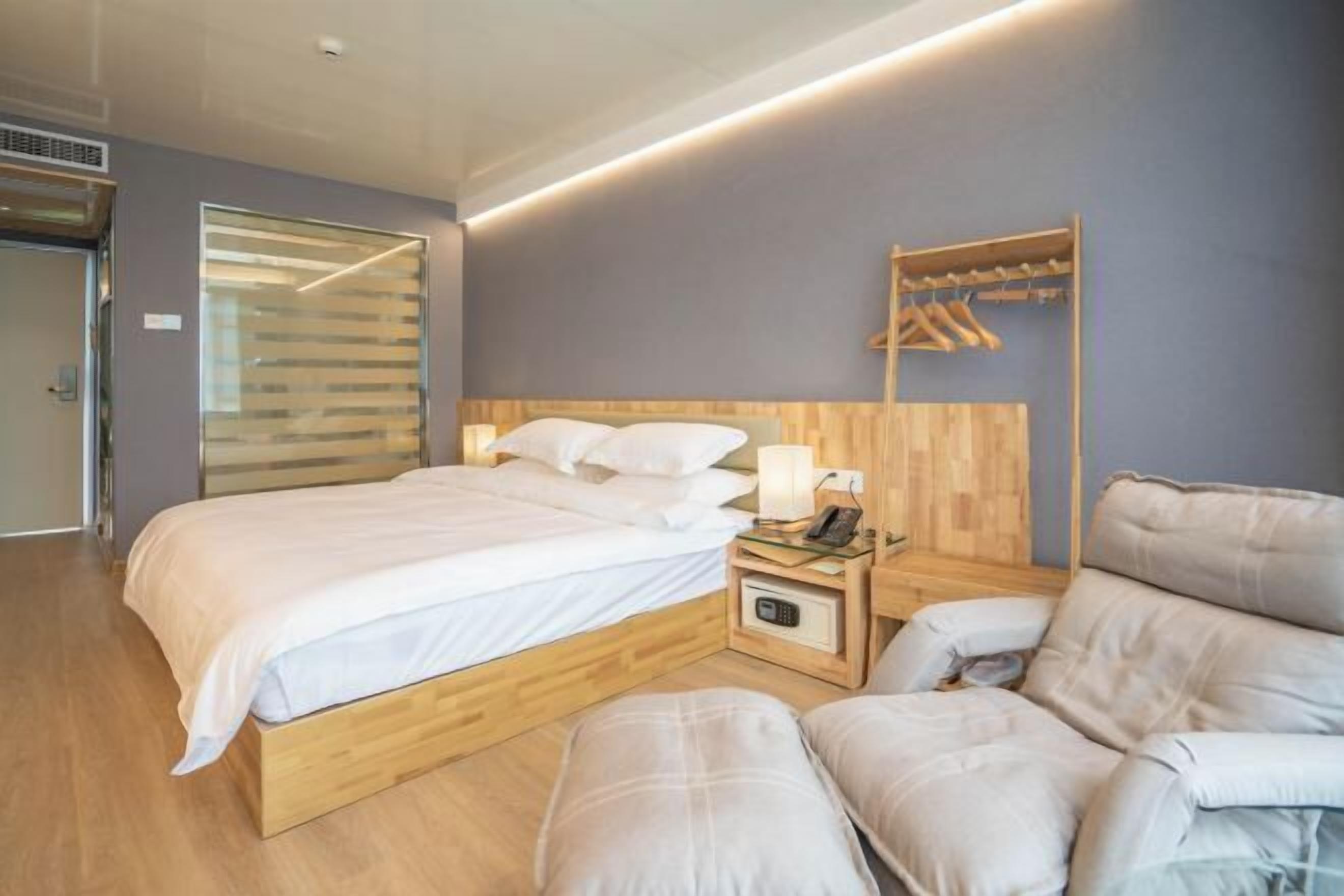A modern hotel room with a wooden bed frame, a bedside table with a lamp, a phone, and a coat rack.