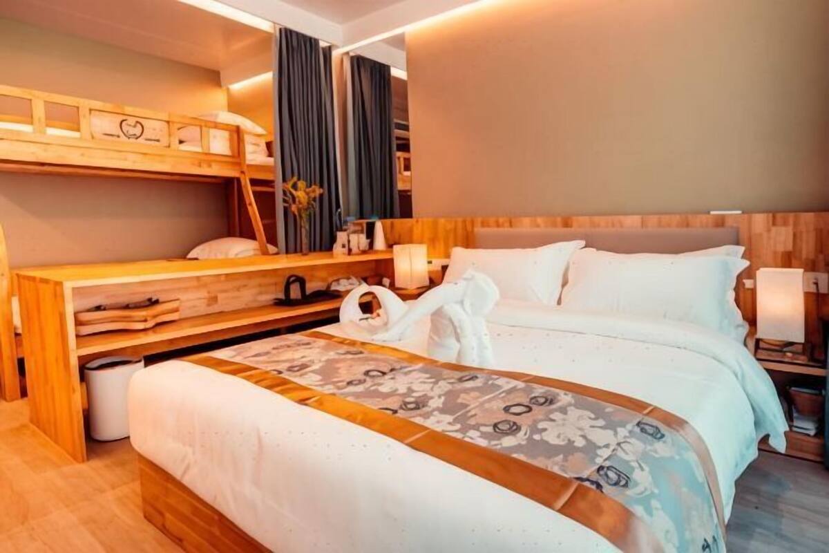 Ein Hotelzimmer mit Etagenbett, einem Einzelbett, einem Nachttisch mit Lampe und einem großen Fenster mit Vorhängen.