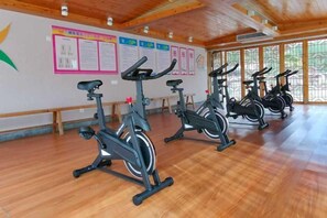 Une salle de sport équipée de vélos d’appartement, dotée d’un plancher en bois et ornée d’affiches illustrant des exercices sur les murs.