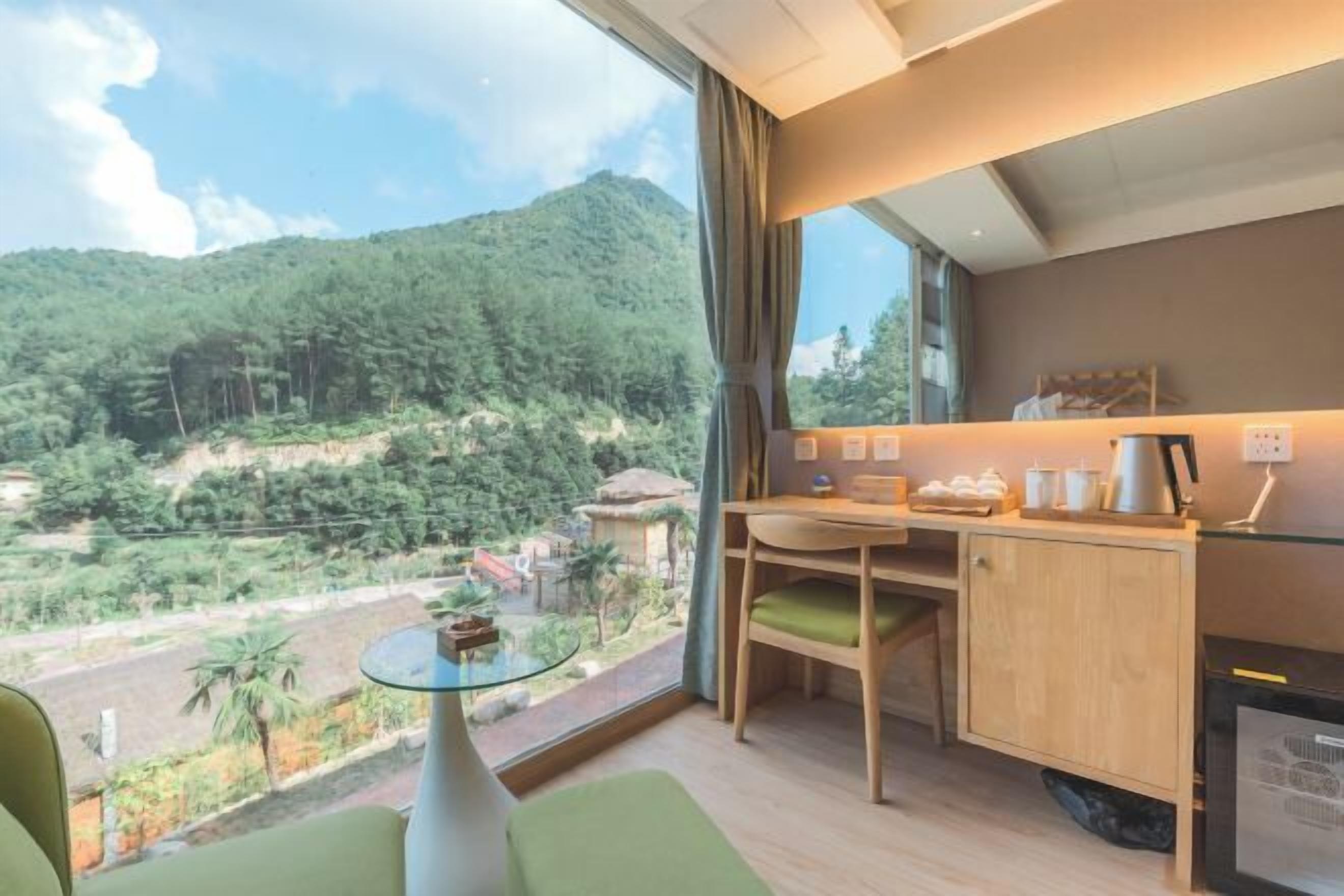 Una habitación con escritorio, silla y una pequeña mesa con superficie de vidrio. Se aprecia una vista panorámica de un paisaje montañoso a través de un ventanal grande.