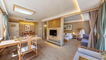 A hotel room with a wooden dining table, a sofa, a TV mounted on a wall, and a bed with a nightstand.