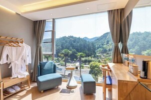 Quarto moderno com uma janela grande, um sofá azul, uma mesa de apoio de madeira e um cabideiro.