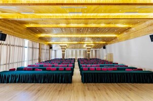 A conference room with rows of tables and chairs, wooden ceiling, and large windows.
