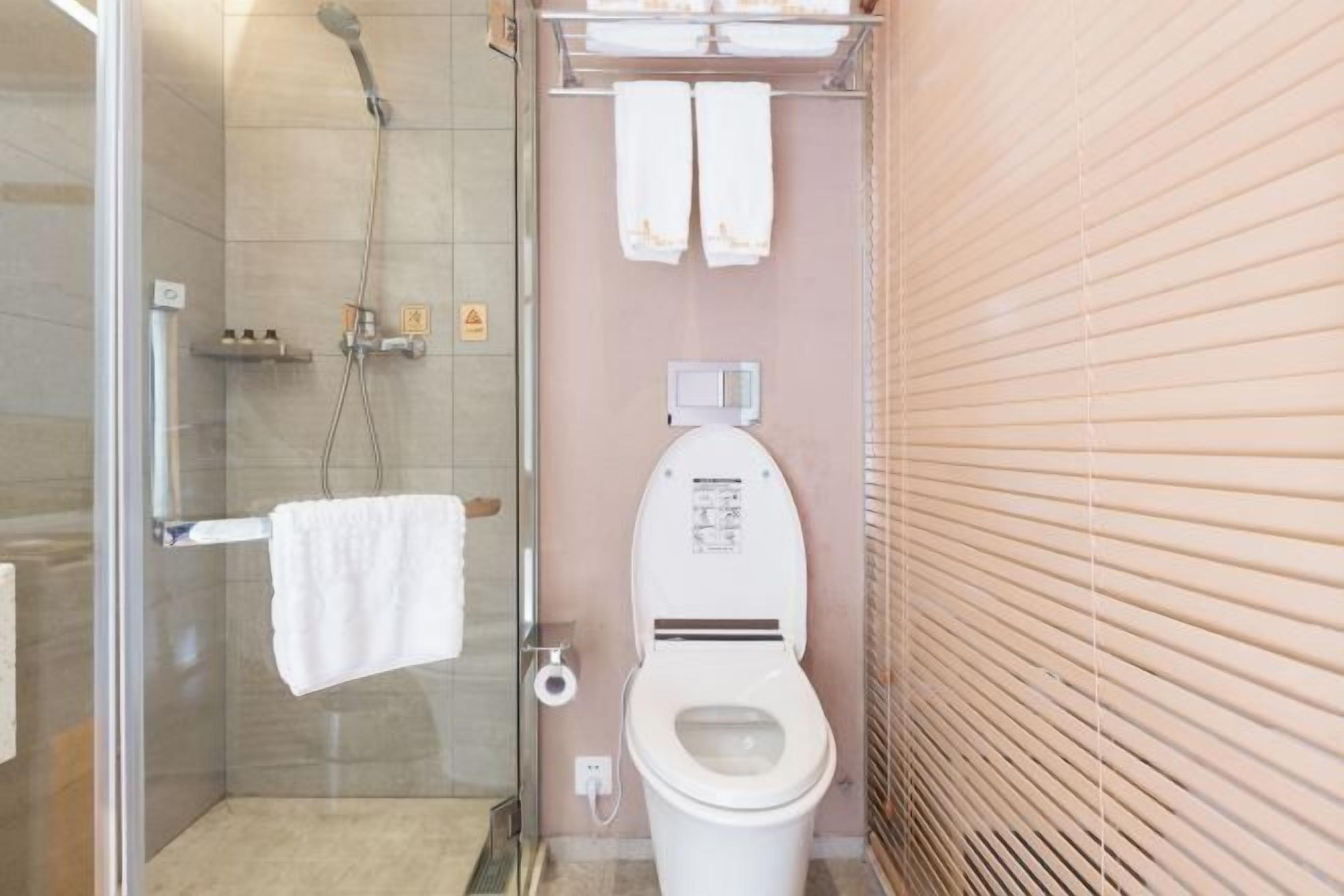 A bathroom with a glass shower enclosure, a toilet, and a towel rack.