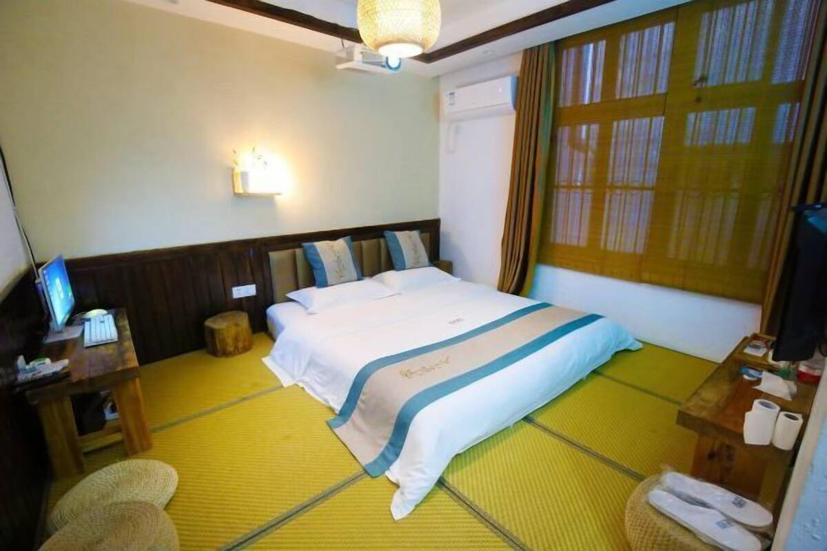 Habitación de hotel con cama, mesita de noche, lámpara, televisión, ventana con cortinas y un futón.