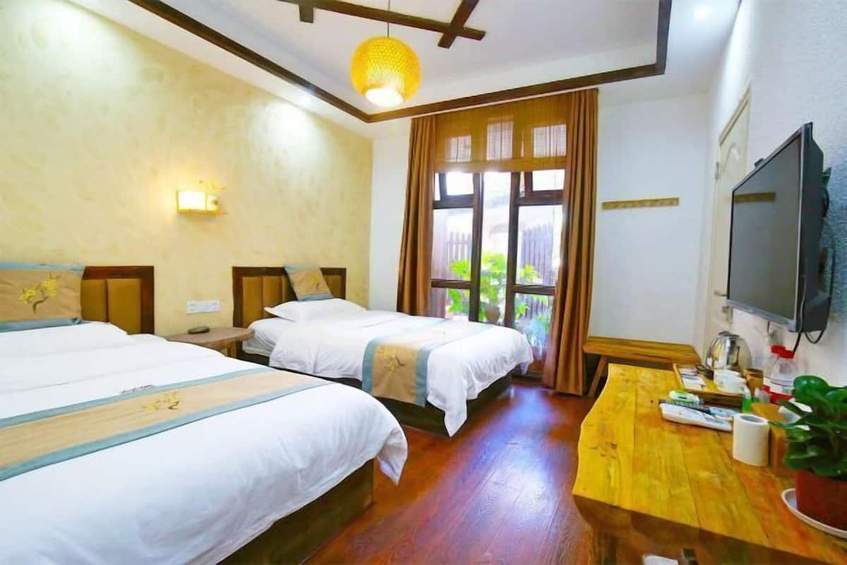 Habitación de hotel con dos camas, un escritorio de madera, televisión y ventana con cortinas.
