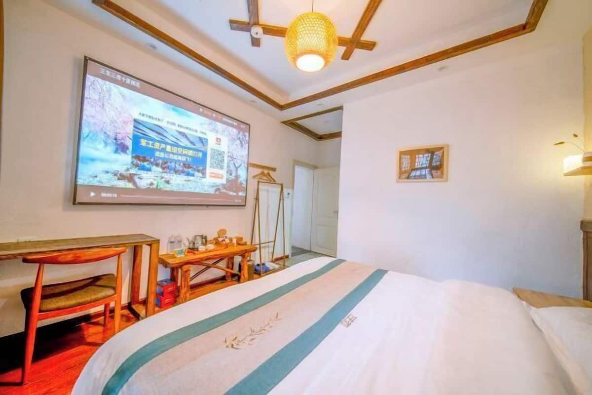 Habitación de hotel con cama, escritorio, silla, televisor montado en la pared y lámpara colgante.