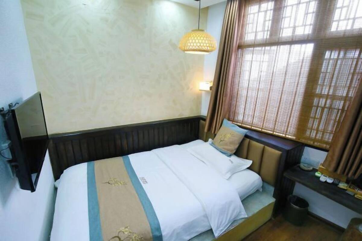 Una cama bien hecha con una colcha a rayas, una lámpara de noche y una ventana con cortinas.