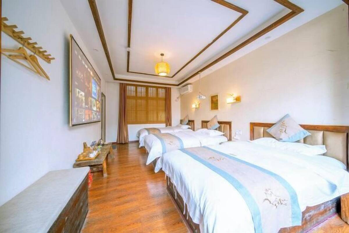 Habitación de hotel con piso de madera, una cama grande con cubrecama azul y blanco, cabecera de madera, televisor montado en la pared y lámpara del techo.