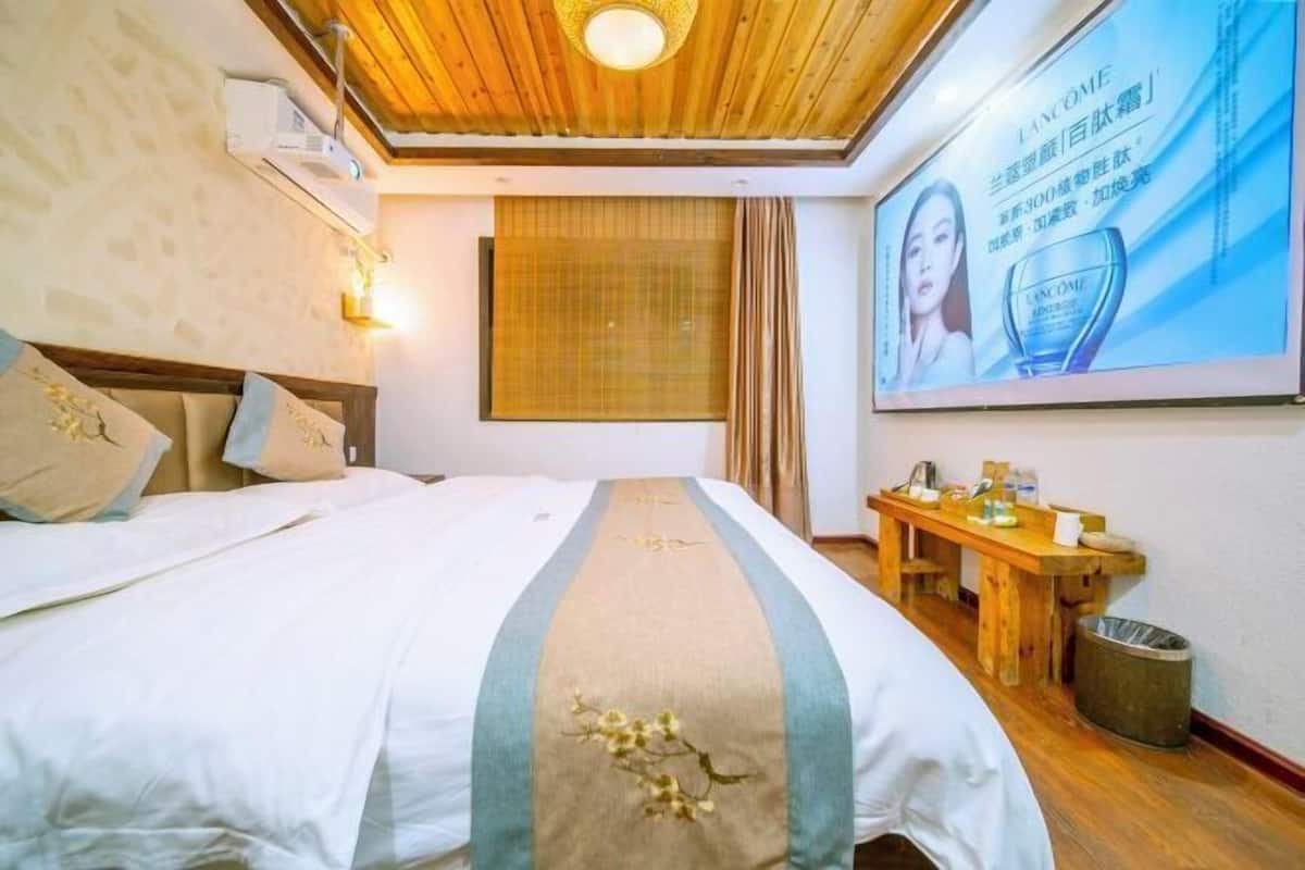 Habitación de hotel con cama, techo de madera, aire acondicionado de pared, ventana con cortinas y una mesa con objetos encima.