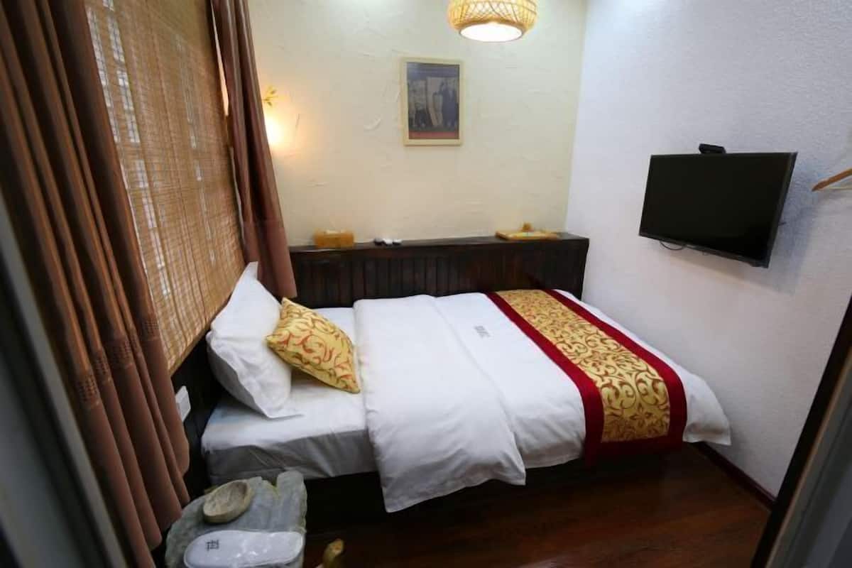 Una habitación pequeña y funcional con una cama individual, un televisor montado en la pared y una mesita de noche con una lámpara.