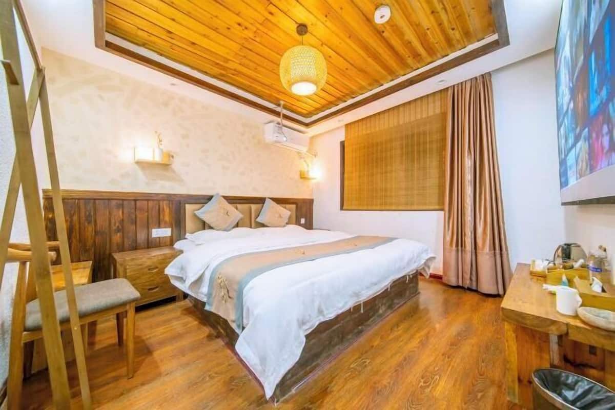 Un dormitorio con techo de madera, una cama con cabecera, una mesita de noche, una silla y una ventana con cortinas.