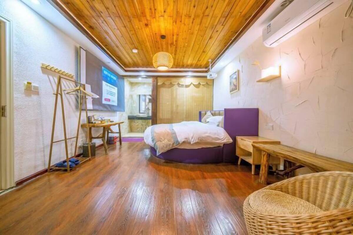 Una habitación con techo de madera, una cama con cabecera morada, un escritorio de madera y una silla de mimbre.