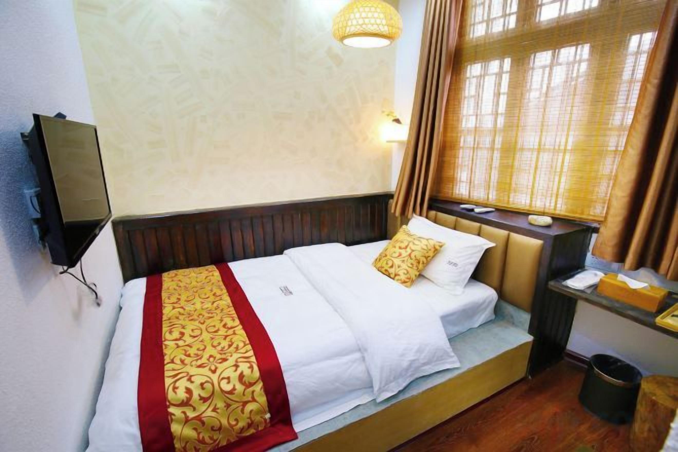 Una habitación de hotel con cama, mesita de noche, lámpara y ventana con cortinas.