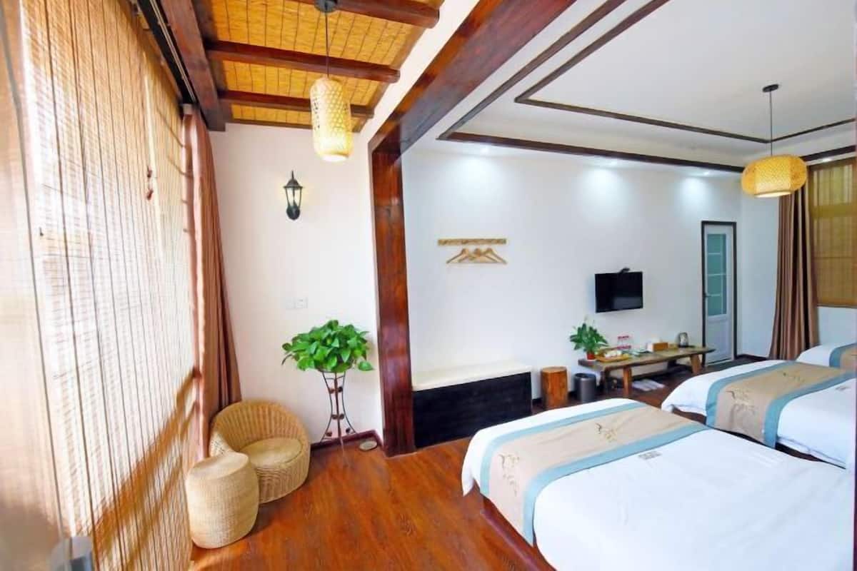 Habitación de hotel con suelo de madera, una cama con colcha azul y blanca, un escritorio con silla, televisión y una planta en maceta.