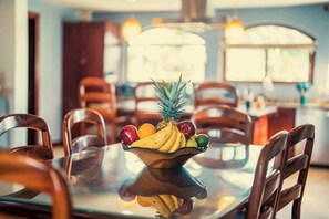 A dining table with a fruit bowl in the center, surrounded by wooden chairs.