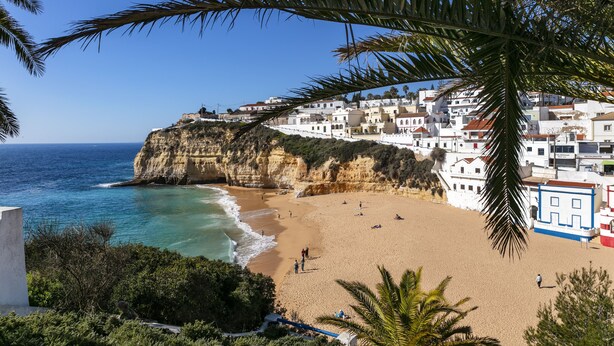 A coastal town with a beach, white buildings, and a cliff overlooking the sea.