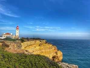 A coastal lighthouse with a red top, situated on a cliff overlooking the sea.