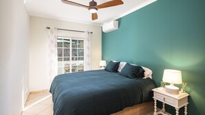 A bedroom with a bed, a nightstand with a lamp, a ceiling fan, and a window with curtains.