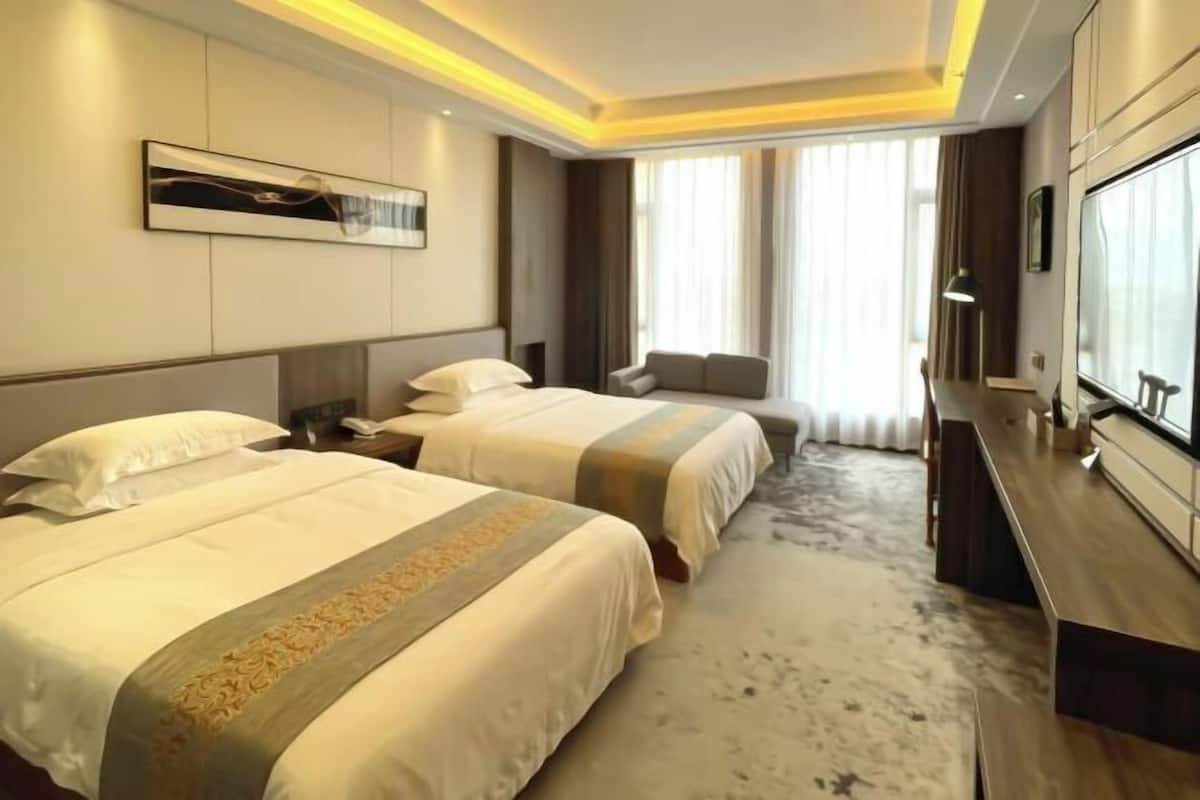 Habitación de hotel con dos camas, un ventanal con cortinas, un televisor de pantalla plana y un escritorio de madera.