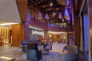 A spacious lobby with a reception desk, seating area, and a high ceiling with hanging lights.