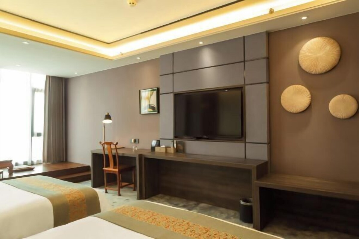 A hotel room with a bed, a desk, a chair, a TV, and decorative wall art.