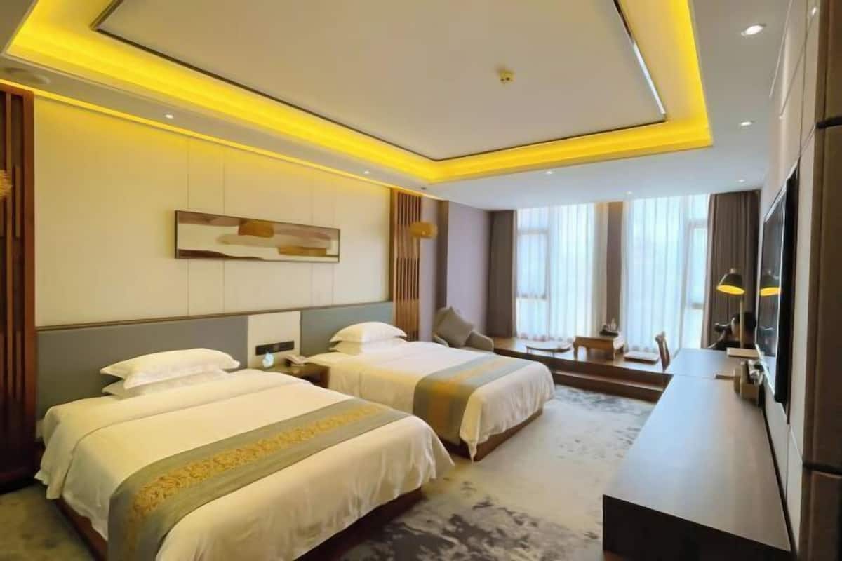 Habitación de hotel con dos camas, un escritorio y un ventanal grande.