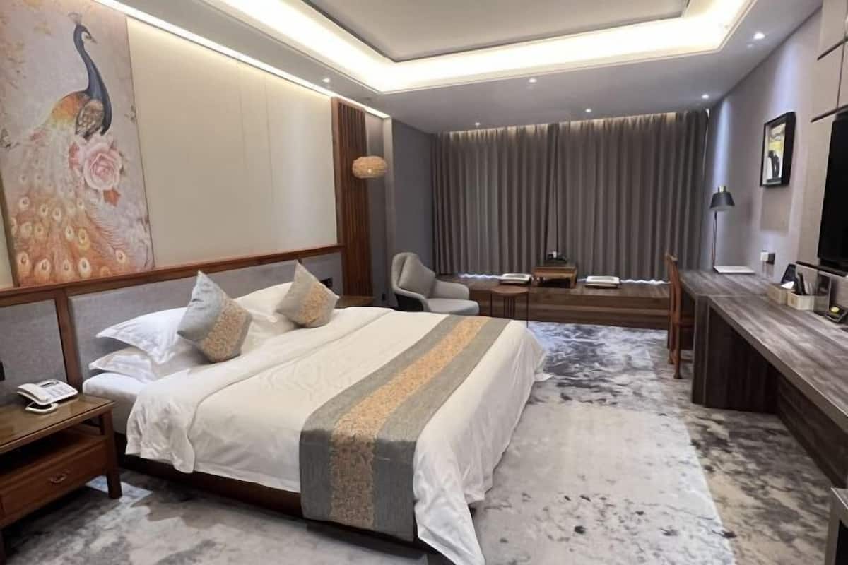 Habitación de hotel con una cama grande, mesita de noche, un escritorio con silla, televisor y un cuadro grande en la pared.